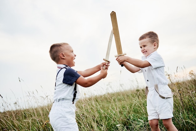 Finge que eres un verdadero maestro. Dos niños divirtiéndose jugando con espadas de madera en el campo