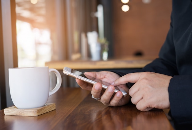 Finger auf Schirm Smartphone auf Hintergrundbretterboden im Caféshop zeigen.