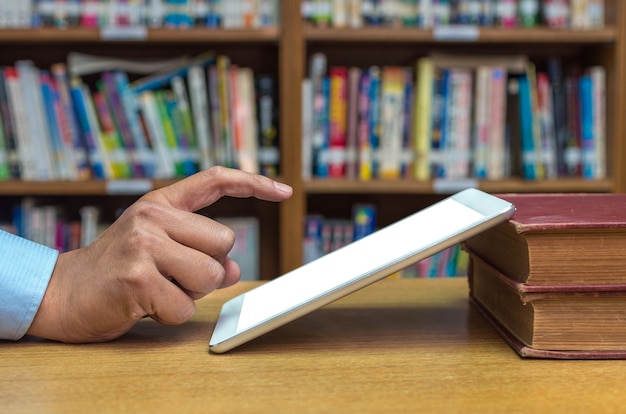 Finger, der auf den Schirm des Tablet-Computers über der hölzernen Tabelle in der Bibliothek zeigt