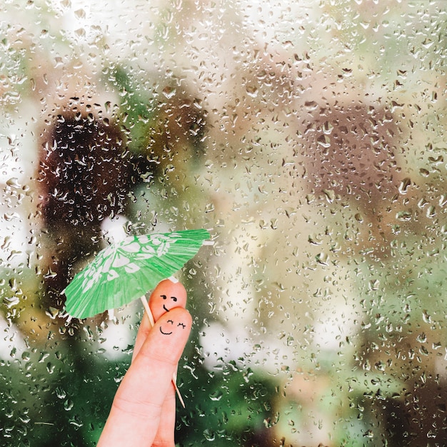 Finger mit Regenschirm nahe Glas mit Regentropfen
