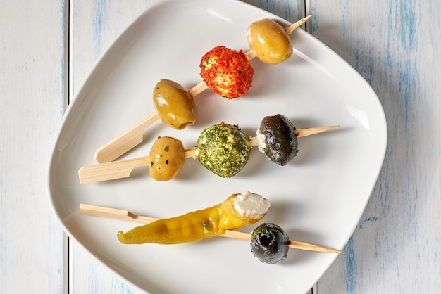 Fingerfood-Sticks mit Oliven und gefüllten Peperoni auf weißem Teller.