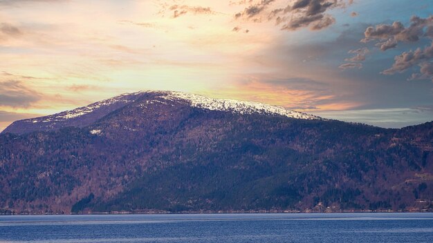 Fiordo con montañas cubiertas de nieve en el horizonte y puesta de sol con nubes brillantes