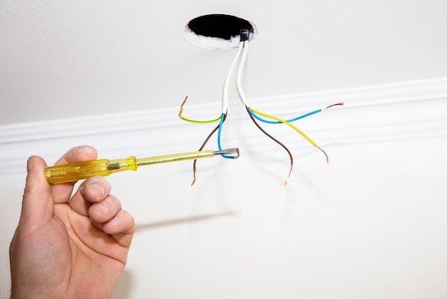 Fios e orifícios para lâmpada no teto Homem segurando chave de fenda Reparos de manutenção de eletricidade no apartamento Restauração dentro de casa