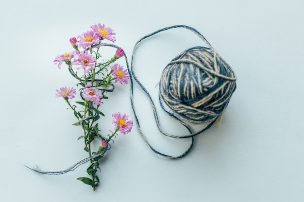 Fios sobre um fundo azul e flores cor de rosa. Fio conceito para tricô