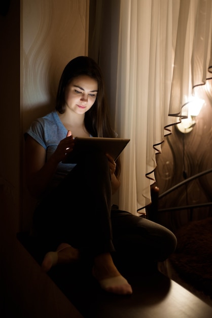 Fique em casa. Trabalhe em casa. Jovem mulher sentada perto da janela e usando o tablet digital em casa.