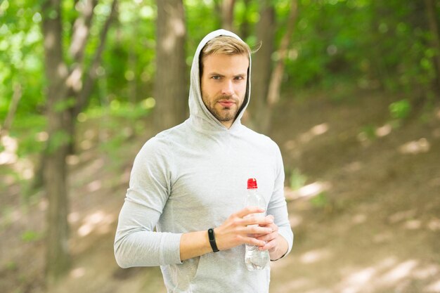 Fique hidratado. Atleta bebe água após o treino no parque. Vitaminas e minerais. Homem atlético esportista segura garrafa de água. As roupas esportivas do homem atleta se preocupam com o equilíbrio da água. Estilo de vida saudável.