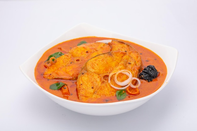 Fisch-Curry_Seer-Fisch-Curry, traditionelles indisches Fisch-Curry, Kerala-Spezialgericht, garniert mit Curryblättern, Zwiebelringen und Malabar-Tamarinde in einer weißen Keramikschale mit weißem Hintergrund