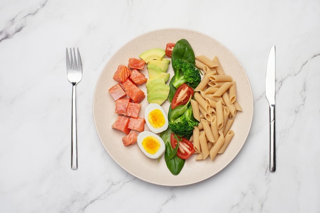 Fisch mit Pasta, Ei und Avocado in einem grauen Teller auf grauem Hintergrund Gesundes Essen Rezept Mittagszeit