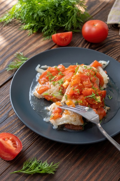 Fisch mit Tomaten und Dill auf dem flachen Teller auf Holztisch