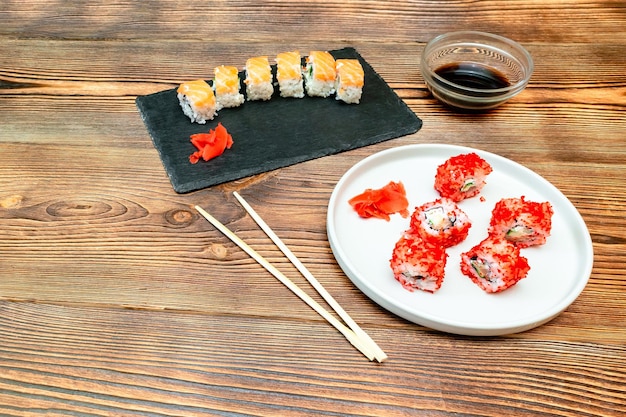 Foto fisch-sushi-rollen mit lachs, ingwer, sojasauce auf schwarzem schneidbrett auf holzgrund meeresfrüchte speisen aus dem restaurant