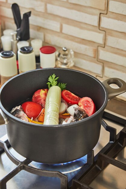 Fischbarsch wird im Kessel mit Tomaten, Karotten und Zwiebeln auf dem Gasherd gedünstet