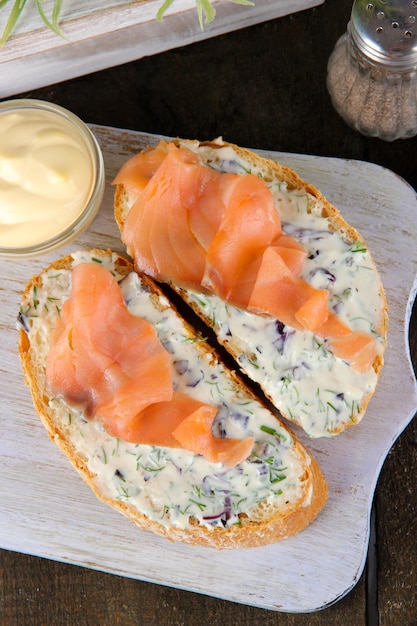 Fischbrötchen und eine Tasse Tee auf Schneidebrett auf Holztisch