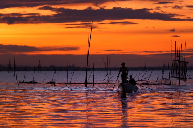 Fischer auf anziehenden Fischen des Bootes mit Sonnenuntergang