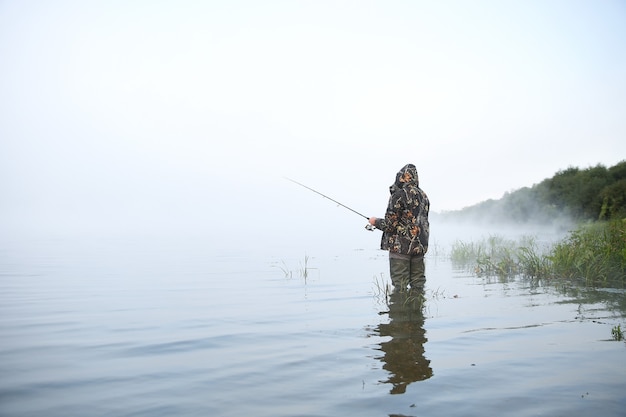 Fischer, der Angelrute auf dem See im Nebel hält