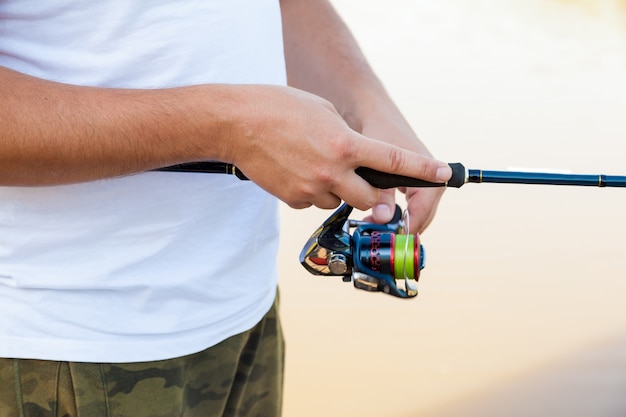 Fischer fängt einen Fisch. Hände eines Fischers mit einer Nahaufnahme der Spinnrute in der Hand.