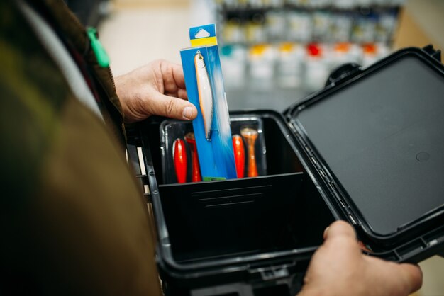 Fischer hält Kiste mit Haken und Kugeln im Angelgeschäft.