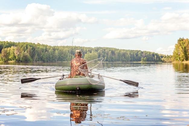 Fischer mit Angelruten fischt in einem Gummiboot vor dem Hintergrund der wunderschönen Natur und des Sees oder Flusses. Camping-Tourismus entspannen Reise aktives Lifestyle-Abenteuer-Konzept