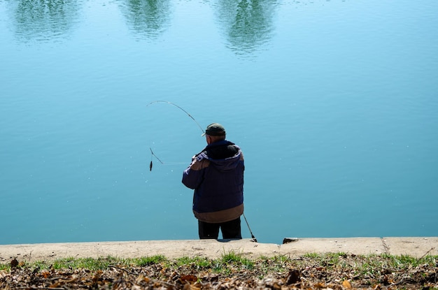 Foto fischer sitzt mit einer angelrute am ufer des sees und fängt fische