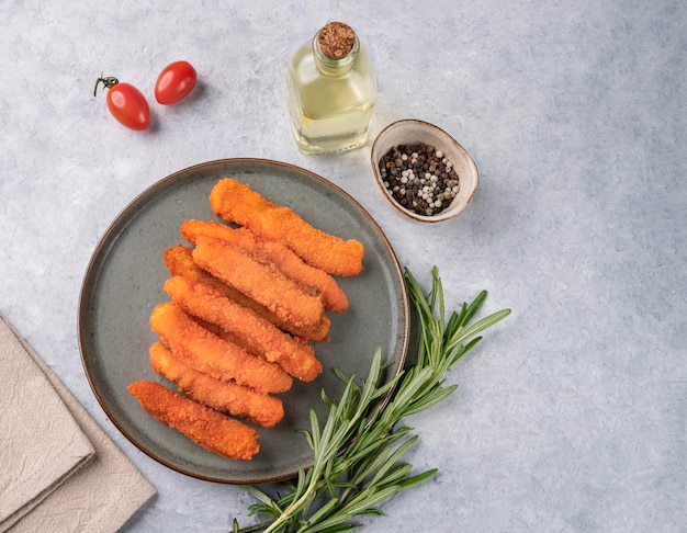 Fischfiletstangen gebraten auf einem grünen Teller mit Rosmarin auf hellem Hintergrund mit Tomaten und Gewürzen Diätetische und gesunde Ernährung