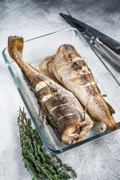 Fischgericht - gebratener Kabeljau mit Kräutern in Auflaufform. Weißer Hintergrund. Ansicht von oben.