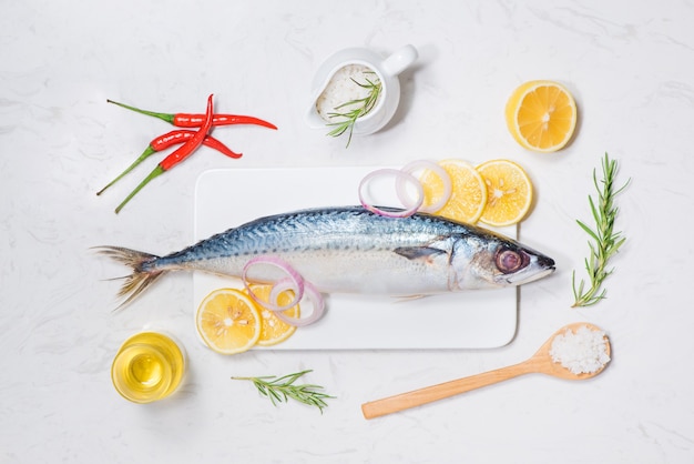 Fischgericht kochen mit verschiedenen Zutaten. Frischer roher Fisch dekoriert mit Zitronenscheiben und Kräutern auf Holztisch.