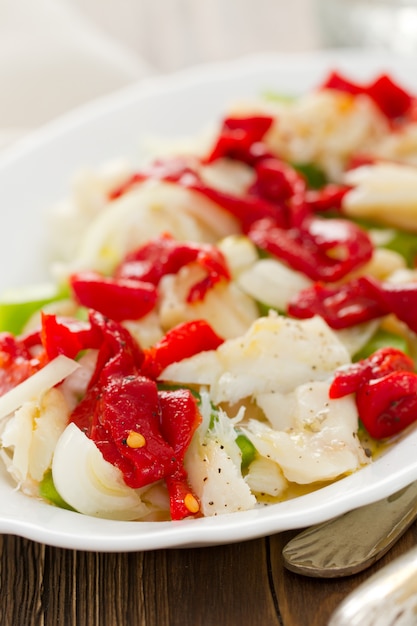 Fischsalat mit rotem und grünem Paprika auf weißem Teller