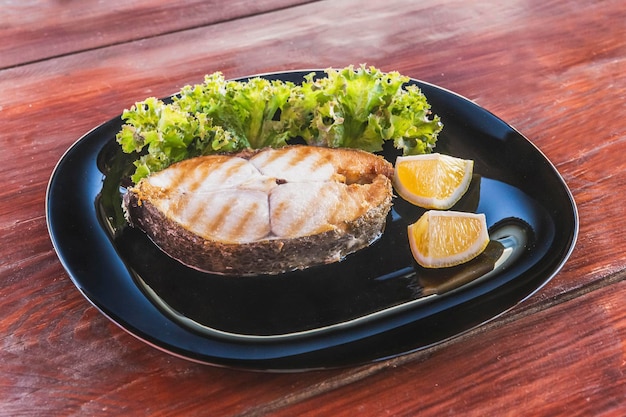 Fischsteak mit Salat auf einem schwarzen Teller