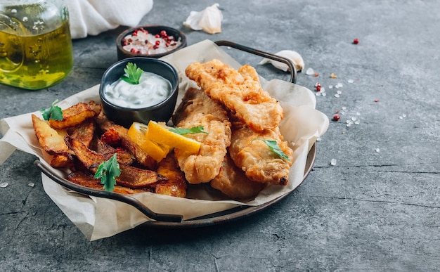 Fish and Chips británico tradicional con salsa tártara sobre fondo de hormigón oscuro. Enfoque selectivo