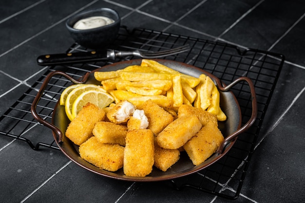 Fish and Chips Fischstäbchen mit Pommes frites in einem Stahlblech mit Sauce Schwarzer Hintergrund Ansicht von oben