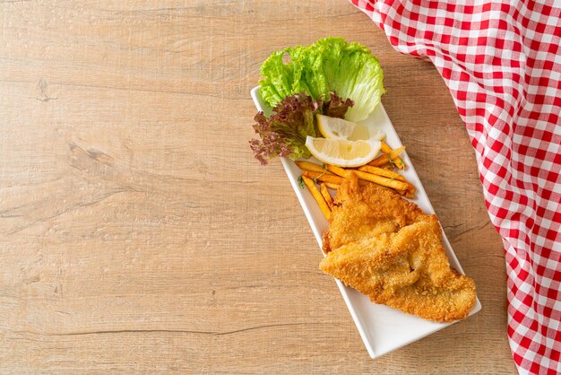 Fish and Chips - gebratenes Fischfilet mit Kartoffelchips und Zitrone auf weißem Teller