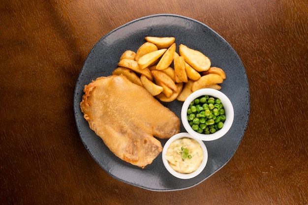 Fish-and-Chips-Teller mit gebratenem Fisch in Scheiben und Kneipentisch-Nahaufnahme mit Remoulade und grünen Erbsen in der Draufsicht