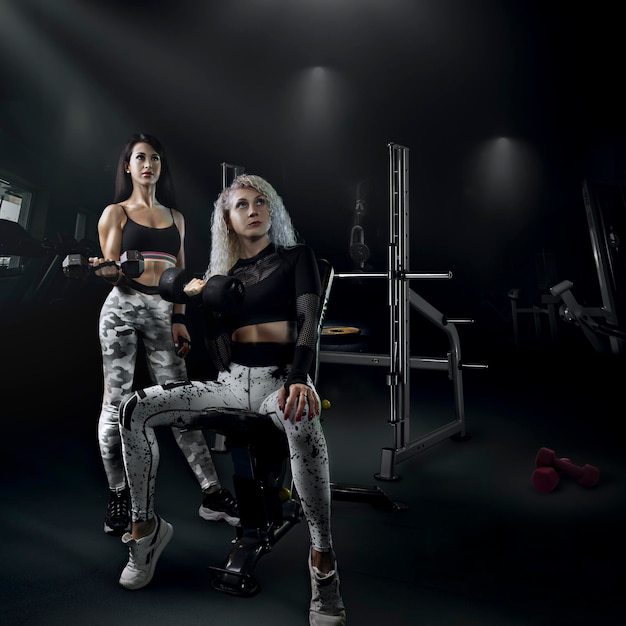 Fisiculturismo fitness, duas lindas garotas praticam esportes junto com um treinador com um corpo bonito e uma figura esguia na foto criativa da academia
