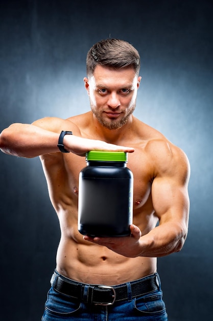 Foto fisiculturista atleta masculino segura um pote de nutrição esportiva em suas mãos, mostrando as poses da câmera em fundo azul