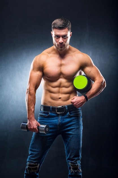 Fisiculturista de atleta masculino tem um pote de nutrição esportiva e halteres nas mãos.