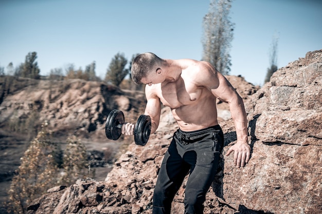 Fisiculturista desportivo com corpo de atleta mostrando seus músculos. Homem musculoso bonito forte posando em paisagens da natureza.