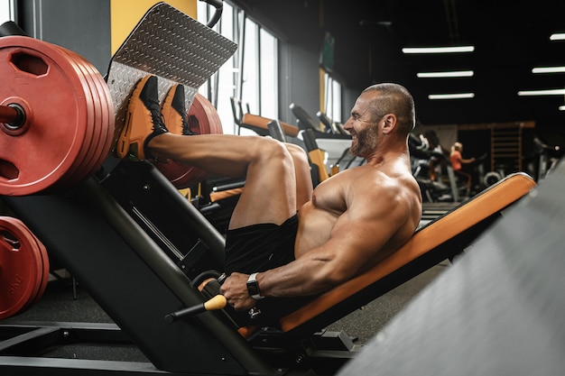 Fisiculturista forte e musculoso fazendo um exercício de leg press sentado em uma academia