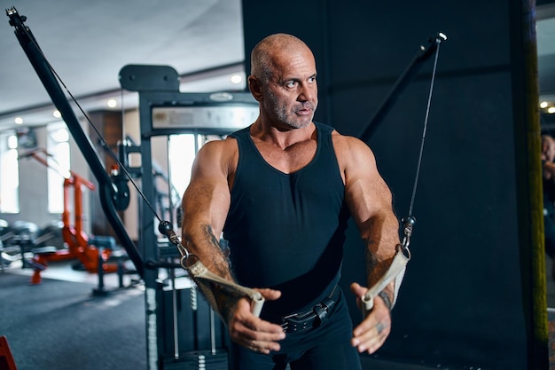 Fisiculturista idoso careca na academia durante o treinamento que é atleta ou instrutor