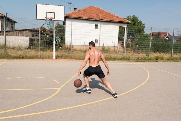 Fisiculturista jogando basquete ao ar livre