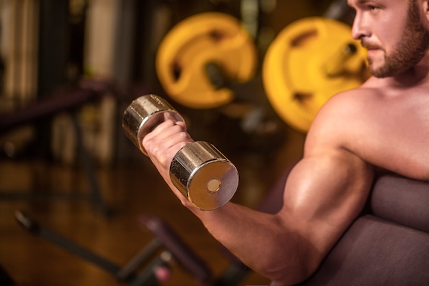 Foto fisiculturista malhando com halteres na academia. homem levantando halteres em uma academia, fazendo exercícios para os músculos. fisiculturista de homem fazendo exercícios com halteres. homem de fitness levantando halteres