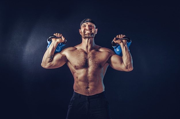 Fisiculturista muscular barbudo agressivo fazendo exercícios para os músculos do ombro, deltóide com kettlebell. tomada