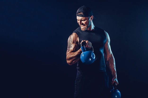Fisiculturista muscular barbudo agressivo fazendo exercícios para os músculos do ombro, deltóide com kettlebell. tomada