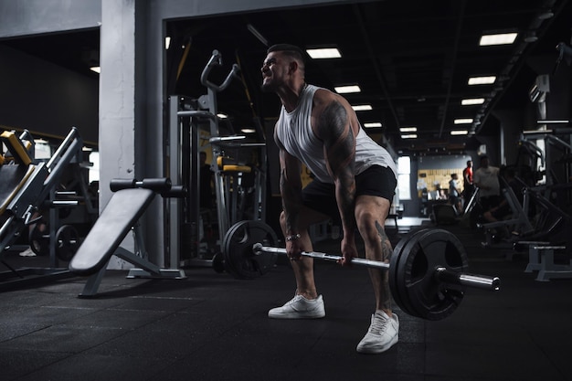 Fisiculturista muscular levantando barra pesada com esforço na academia