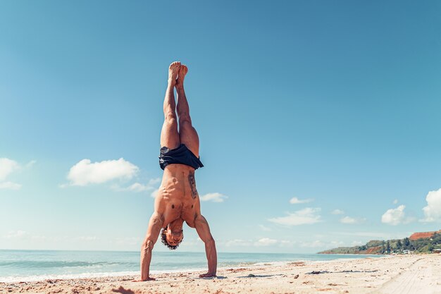 Fisiculturista musculoso e fitness homem com um torso nu em pé de braço dado na praia