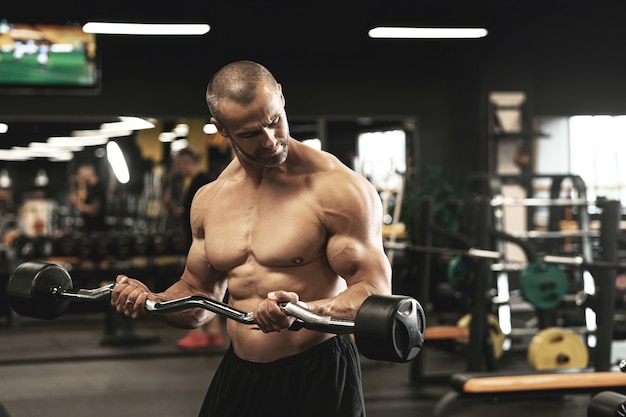 Foto fisiculturista musculoso fazendo bíceps com uma barra durante seu treino na academia