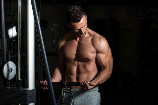 Fisiculturista musculoso jovem fazendo exercícios de peso pesado para bíceps na máquina de cabo