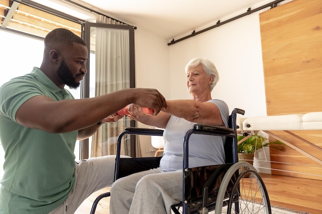 Fisioterapeuta afro-americano ajudando mulher idosa caucasiana a fazer exercícios com halteres
