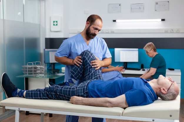 Fisioterapeuta ajudando velho com lesão na perna a se recuperar na clínica de cinoterapia. quiroprático dando suporte a paciente aposentado com dor nos joelhos e pressão muscular para recuperação.