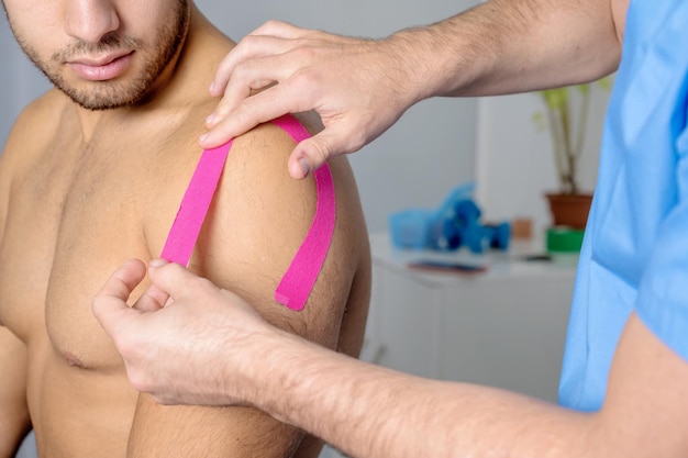 Fisioterapeuta aplicando cinta de kinesio en el hombro del paciente masculino kinesiología fisioterapia rehabilitación ...