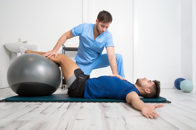 Fisioterapeuta ayuda a apuesto joven paciente con ejercicios de pilates