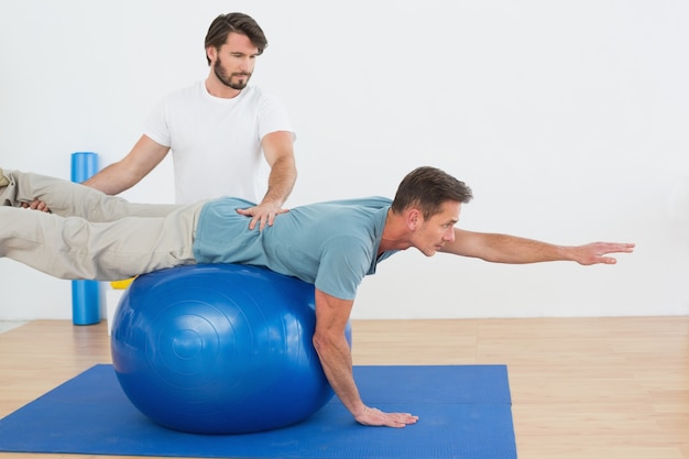 Fisioterapeuta ayudando a hombre joven con pelota de yoga